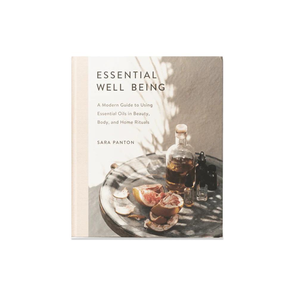 Essential Well Being book with a light cover, featuring essential oils, grapefruit, and shadows on a tray.