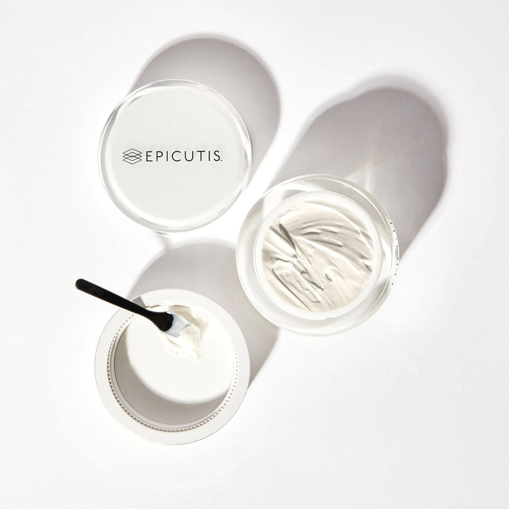 Epicutis Hyvia Crème in a white jar with a black spatula, lid with logo, on a white surface.