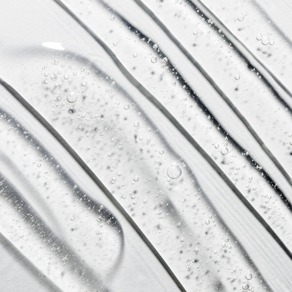 Clear gel cleanser texture with small bubbles, swirled diagonally on a white surface.