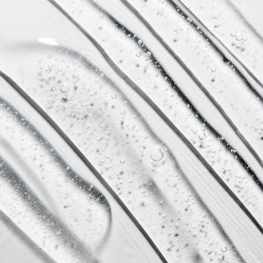 Clear gel cleanser texture with small bubbles, swirled diagonally on a white surface.