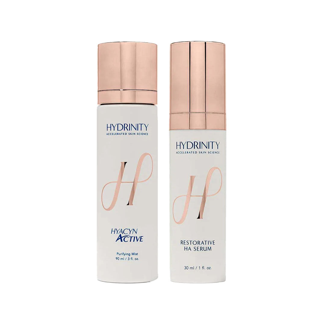 Two white Hydrinity skincare bottles with rose gold caps: HYACYN ACTIVE Purifying Mist and RESTORATIVE HA SERUM.