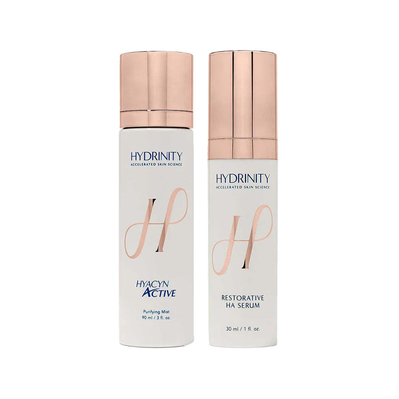 Two white Hydrinity skincare bottles with rose gold caps: HYACYN ACTIVE Purifying Mist and RESTORATIVE HA SERUM.