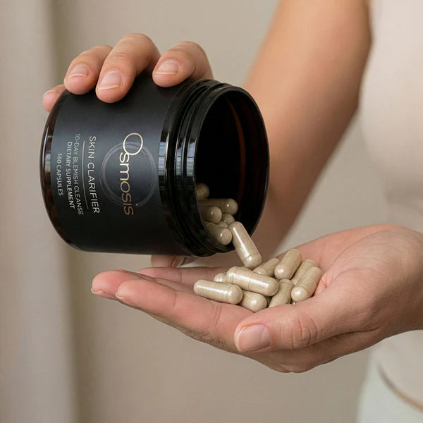 Hands pouring tan Skin Clarifier capsules from a dark brown Osmosis jar into a palm.