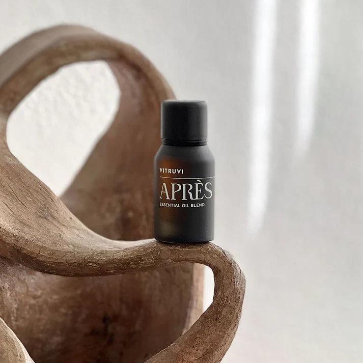Vitruvi Après Essential Oil Blend in a small, dark brown bottle with a black cap, resting on a rustic terracotta pot.