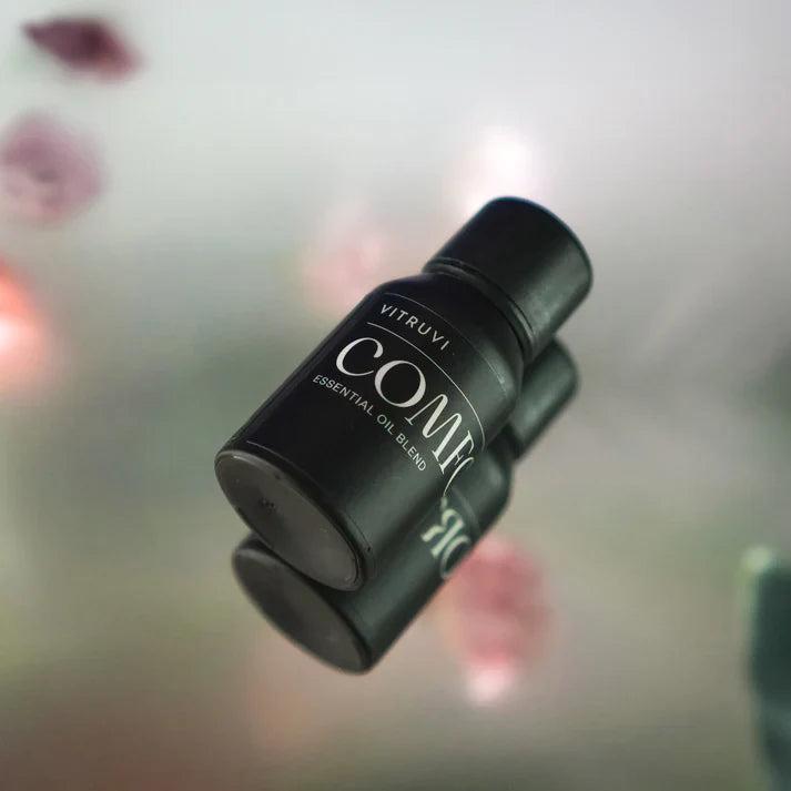 Vitruvi Comfort Diffuser Blend in a small, matte black bottle with white text, reflected on a glossy surface.