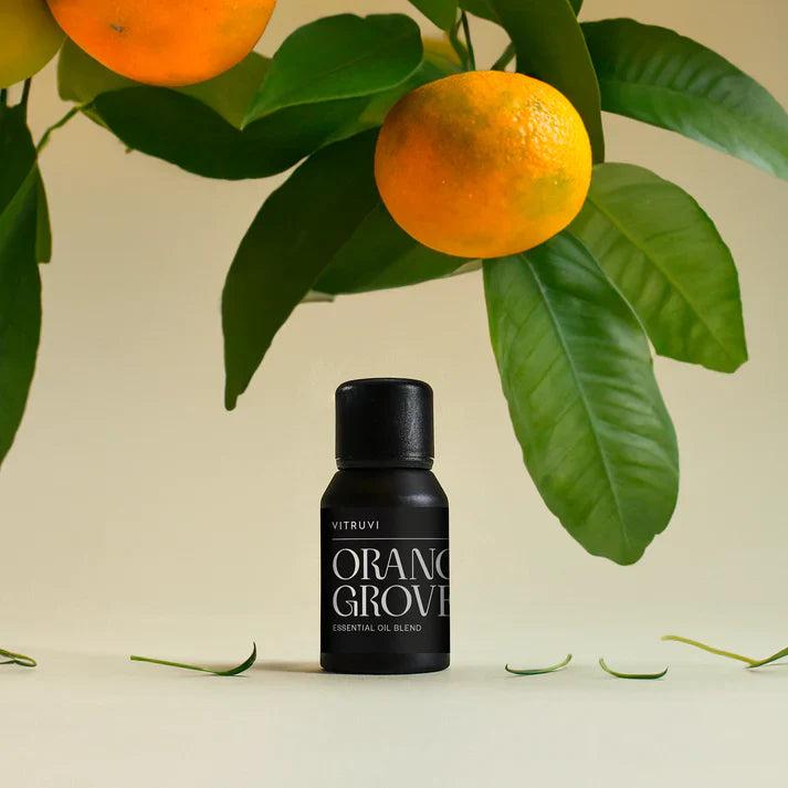 Vitruvi Orange Grove essential oil blend in a small black bottle, with fresh oranges and green leaves.
